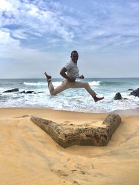 Man jumping at beach against sky