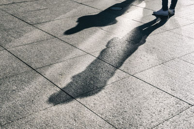 Low section of person standing on footpath with shadow