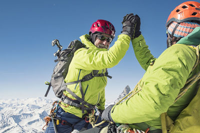 Hikers giving high-five while climbing mountain against clear blue sky