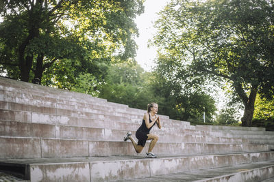 Determined woman practicing lunges on steps at park