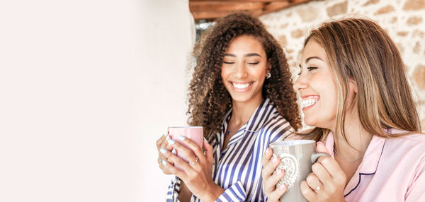 Close-up of smiling women holding coffee cup sitting at home