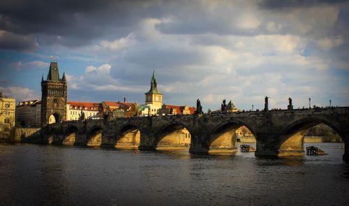 Arch bridge over river by buildings against sky