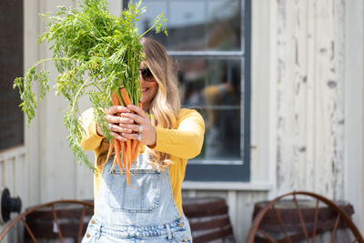 Woman holding carrots while standing against house