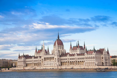 Hungarian parliament building by danube river against sky in city