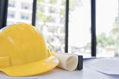 Close-up of yellow hardhat by blueprint at desk in office