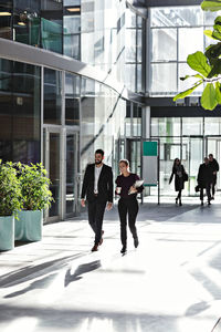 Full length of smiling business coworkers talking while walking in atrium