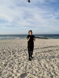 Full length of man standing on beach against sky, juggling