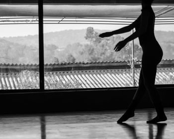 Silhouette woman dancing on floor by glass window in studio