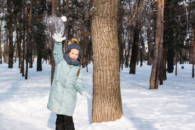 A cheerful girl in warm clothes throws a snowball in the winter forest. walk outdoors.