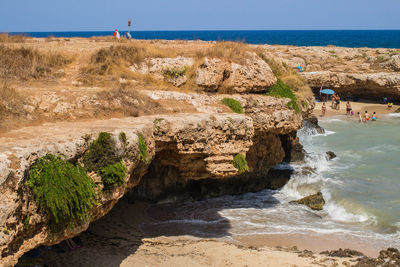 People standing on rock by sea against clear sky