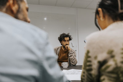 Businessman with hand on chin looking at colleagues in board room