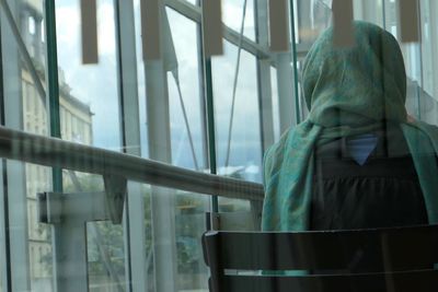Rear view of woman on chair seen through glass at railroad station
