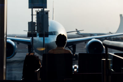 Rear view of man looking at airplane while sitting in airport