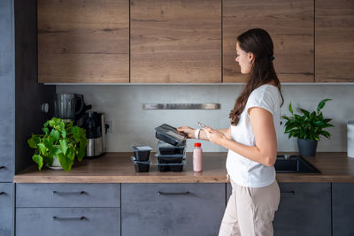 Side view of young woman using mobile phone while standing in kitchen