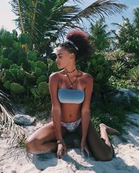 Young woman in bikini while standing on tree against sky