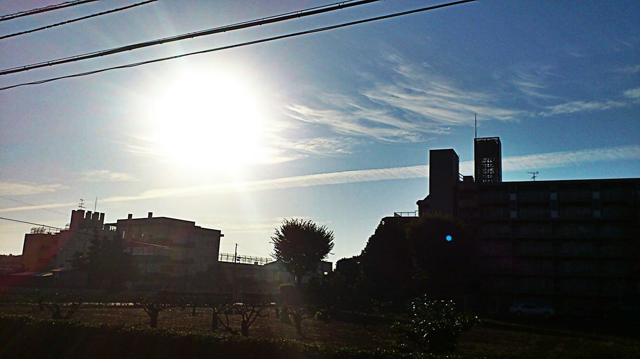 building exterior, architecture, built structure, sun, sky, silhouette, low angle view, sunlight, city, sunset, building, sunbeam, power line, lens flare, cable, cloud - sky, cloud, residential building, outdoors, electricity pylon