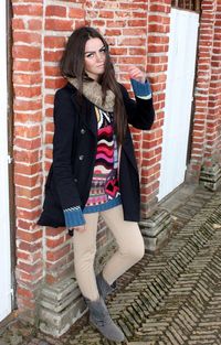 Smiling young woman standing against brick wall