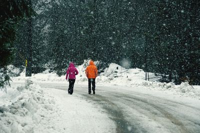 Rear view of two people walking on snow covered landscape