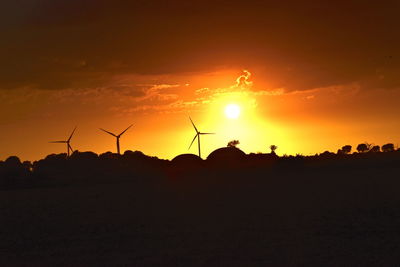 Silhouette wind turbines on field against sky at sunset