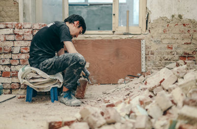 A young man cleans bricks with an axe.