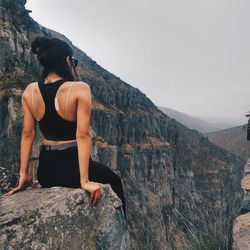 Woman sitting on rock looking at mountain against sky