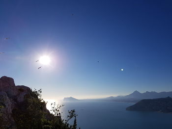 Scenic view of sea and mountains against bright sun