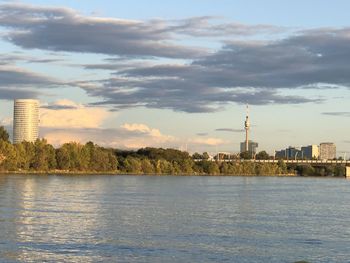 View of buildings by river against cloudy sky