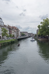 View of city at waterfront against cloudy sky