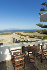 Empty chairs and table at beach against clear sky