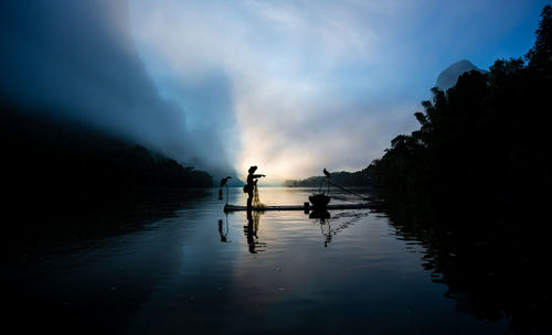 Silhouette people on lake against sky