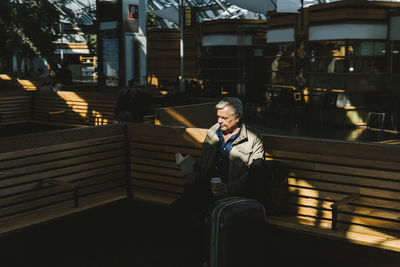 Businessman reading book while sitting on bench at railroad station