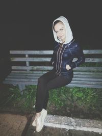 Portrait of young woman standing against wall at night