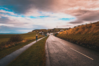 Road amidst field against sky during sunset
