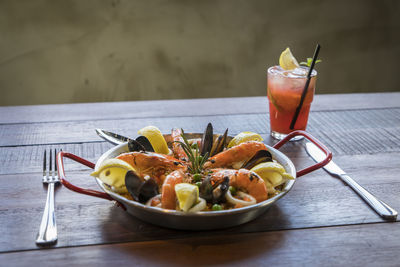 High angle view of paella served in bowl with drink on wooden table