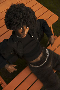 Fashionable non-binary person with curly hair sitting on bench