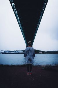 Rear view of woman standing under bridge over river against clear sky