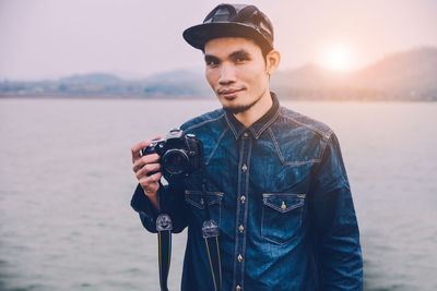 Portrait of man photographing by sea during sunset