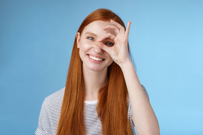 Woman gesturing over eye against blue background