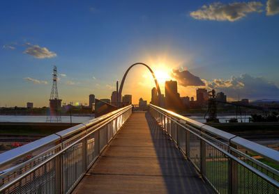 Footbridge over city against sky during sunset