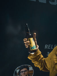 Close-up of hand holding bottle against black background