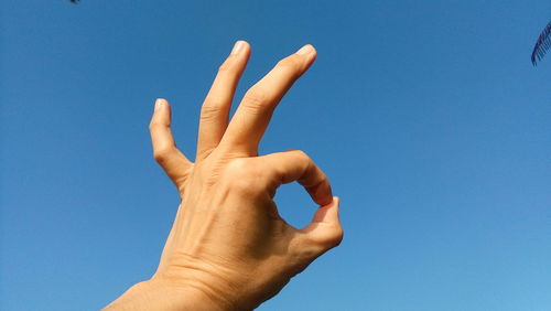 Close-up of hand showing ok sign against clear blue sky