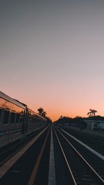 Railroad tracks against clear sky at sunset