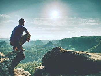 Sit on the edge. man in sports clothes sit on sharp cliff and enjoying far view. misty hilly valley