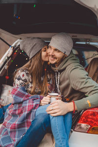 Smiling couple embracing while sitting in car trunk
