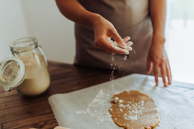 Midsection of a woman sprinkling dough with flour before rolling