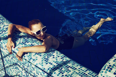 A vintage photo of a woman in a black swimsuit and white sunglasses swimming in the pool