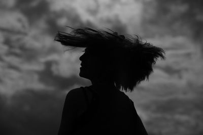 Close-up of silhouette young woman shaking head against cloudy sky during sunset