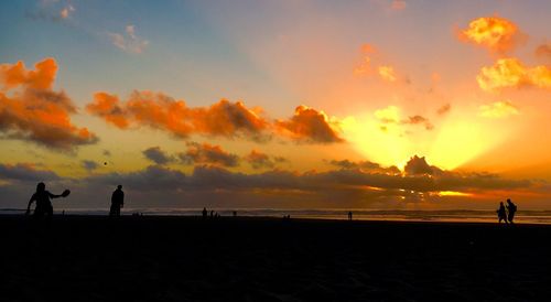 Silhouette people at beach against sky during sunset