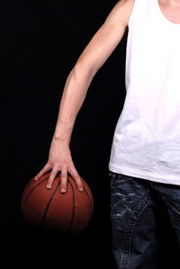 Midsection of woman holding ball while standing against black background