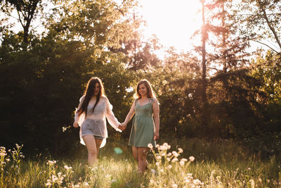 Happy lesbian couple holding hands while walking in forest in summer